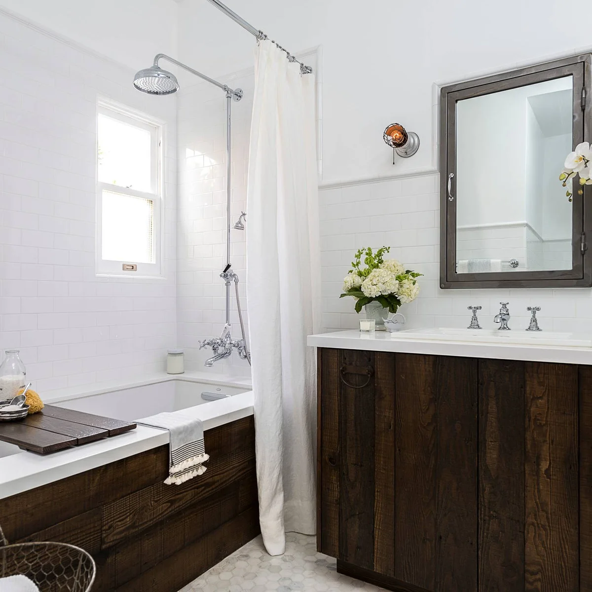 A dark wood vanity and matching bath apron contrast with white wall tile, a pale shower curtain and traditional chrome fittings.