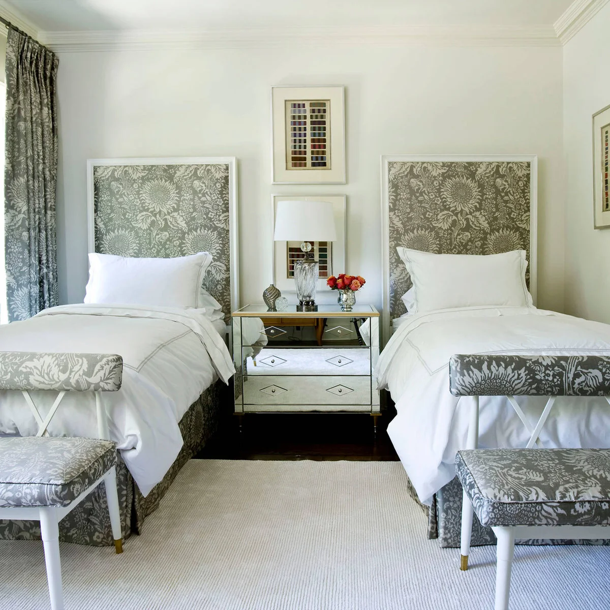 Two white beds with tall gray floral headboards, matching chairs and a mirrored shared chest