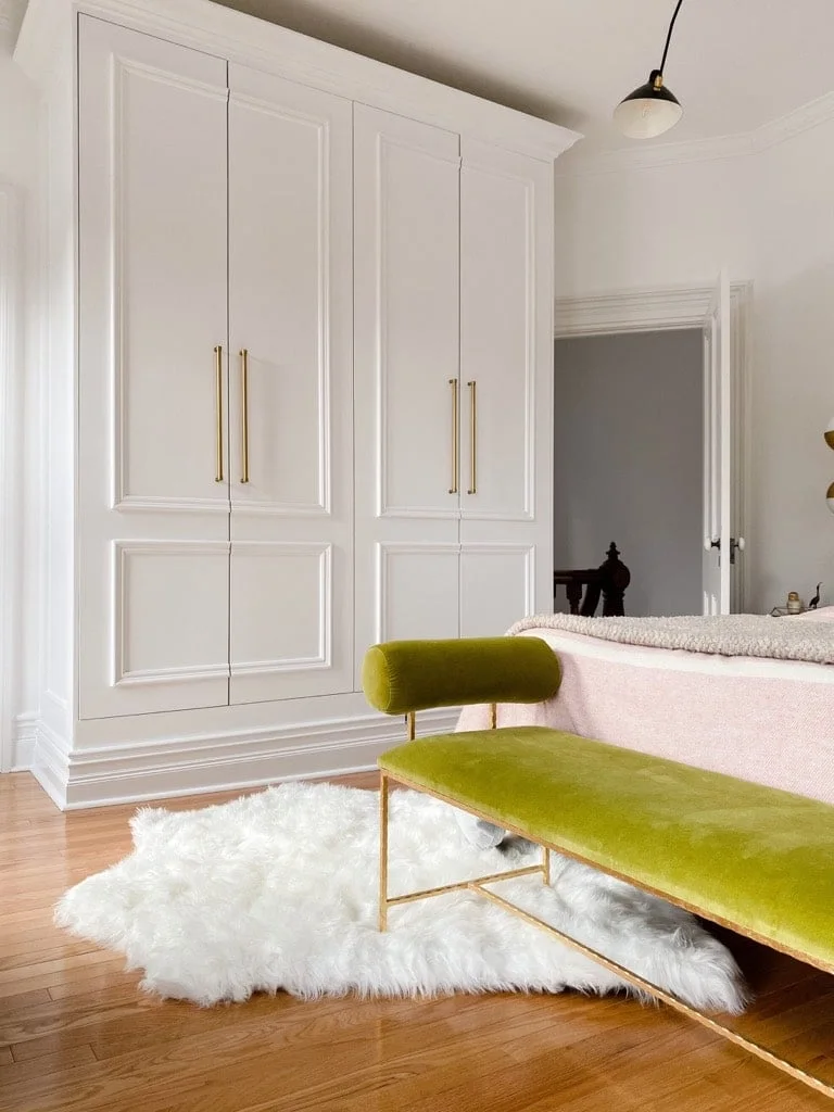 White paneled PAX wardrobe with long gold-colored handles beside a pale bed and green bench