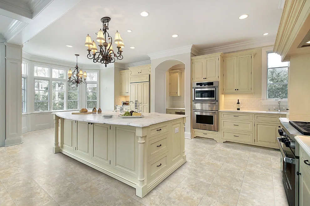 Pale cream cabinetry surrounds a large island beneath decorative ceiling lights