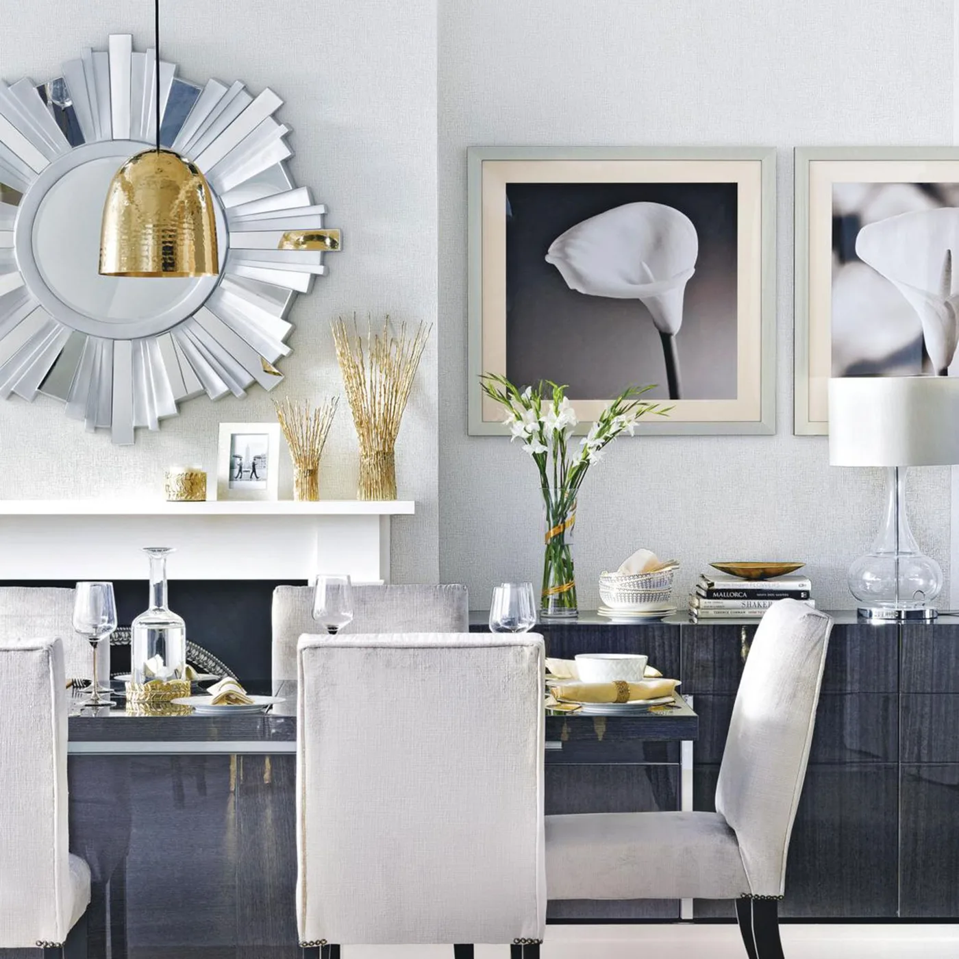 Gold-toned dome pendant above a dark dining table with pale chairs and a silver sunburst mirror