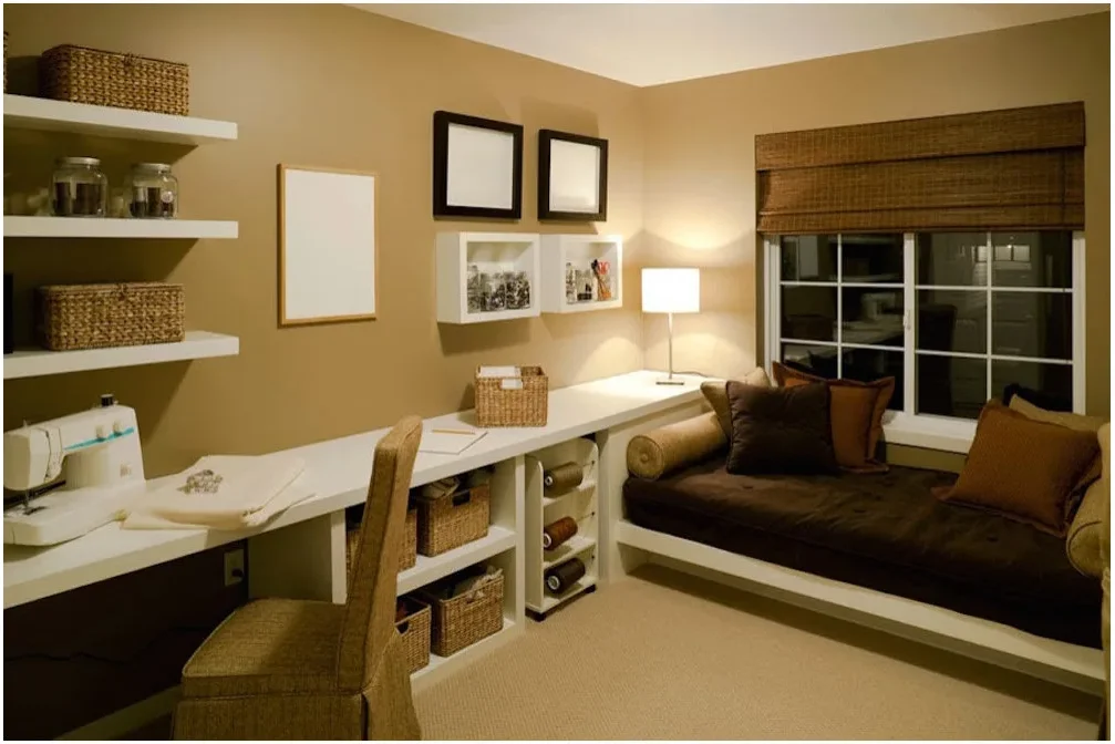 A white sewing counter with a machine and supply shelves runs beside a dark-cushioned daybed below a window.