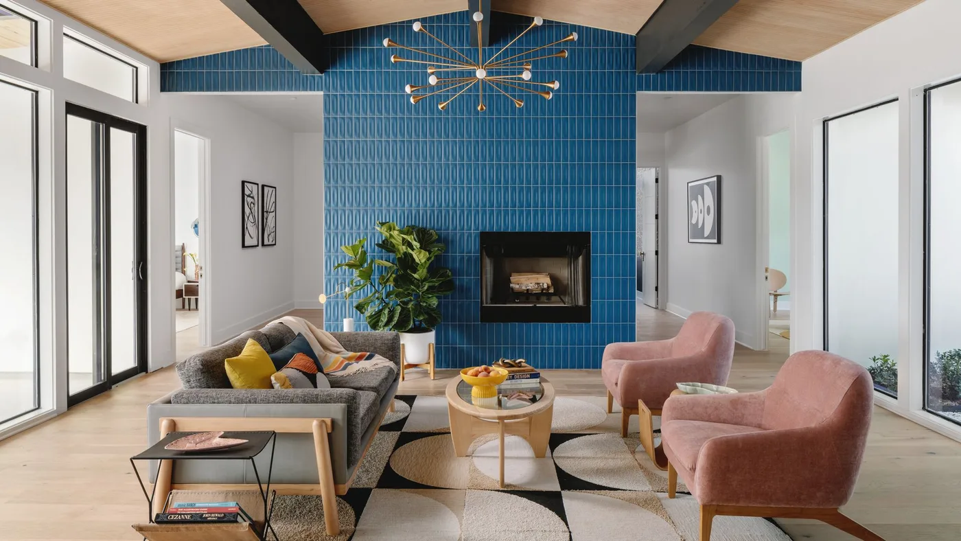 Tall blue vertically tiled fireplace wall under wood ceiling with gray sofa and pink chairs