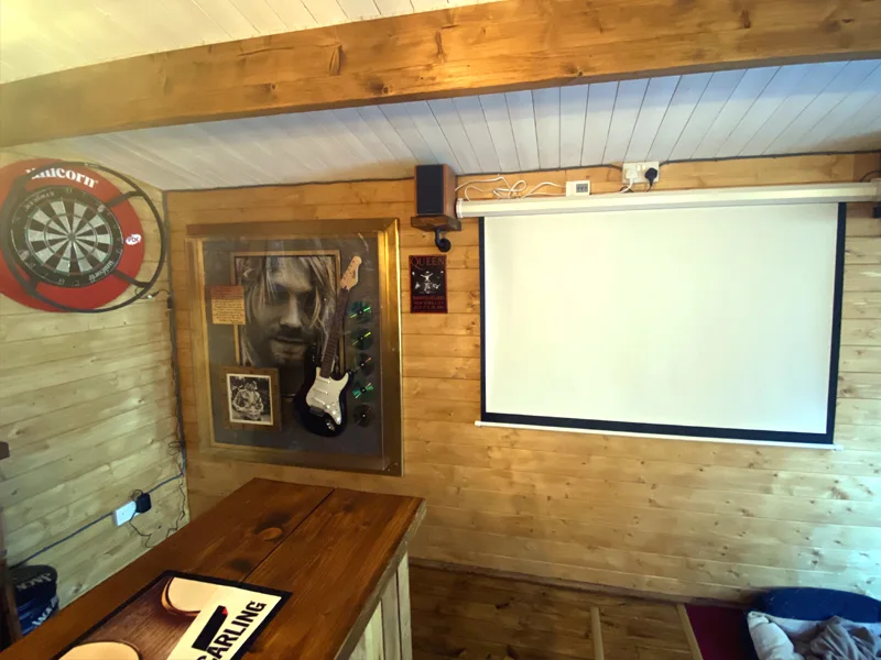 Wood shed pub wall with a dartboard, projection screen and narrow counter below