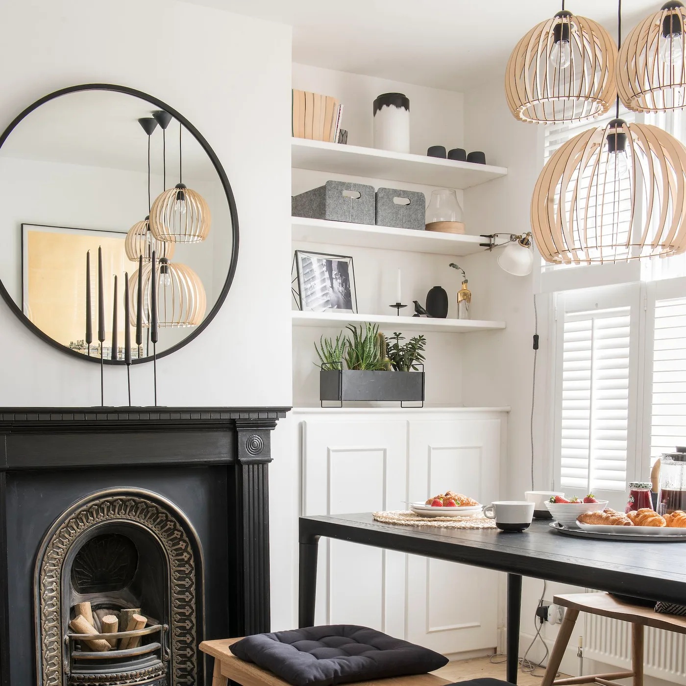 Large black round mirror above a dark fireplace beside a dining table with open wood-toned pendant shades