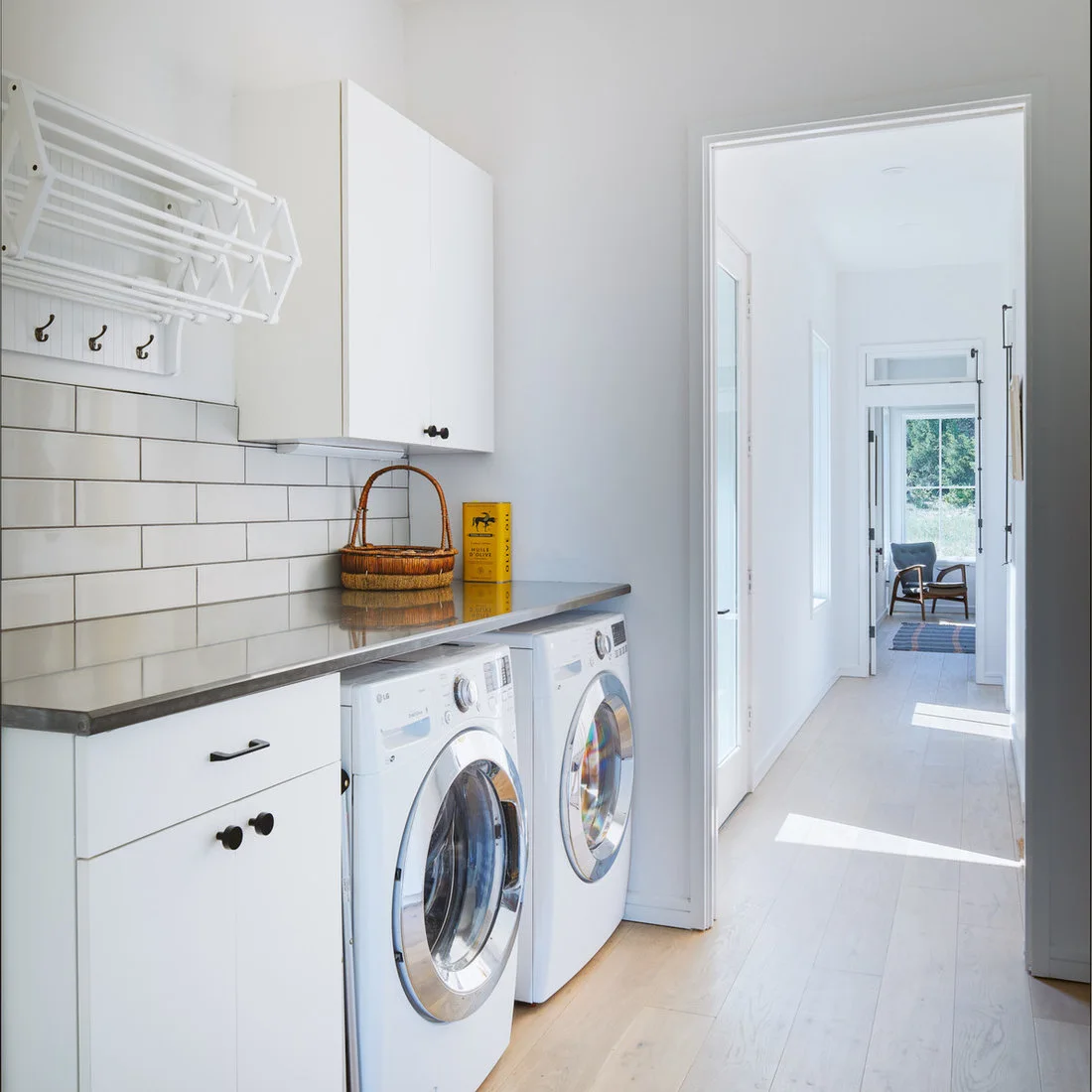 White cabinets and a gray counter sit over two laundry machines beside a folding wall-mounted drying rack.