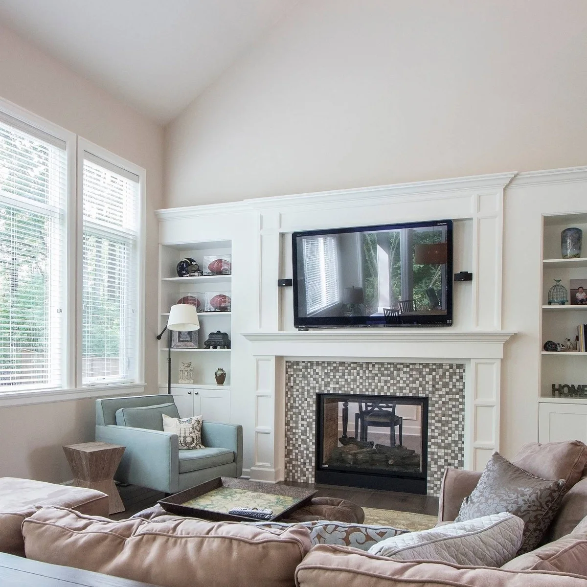 A television in a white trimmed recess above a mosaic fireplace, with built-in shelves and a pale blue armchair.