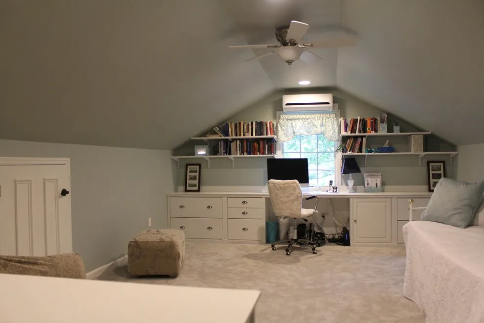 A desk sits beneath a pitched end wall beyond a small attic sitting area