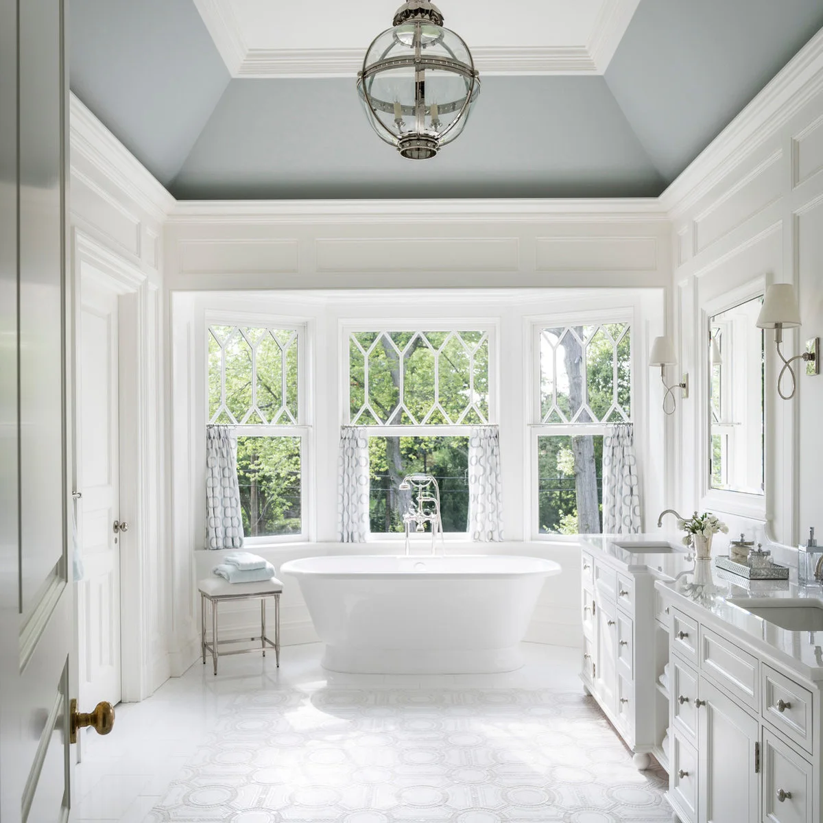 Pale cafe panels with a gray geometric repeat hang below decorative diamond-patterned upper panes in a white bathroom.