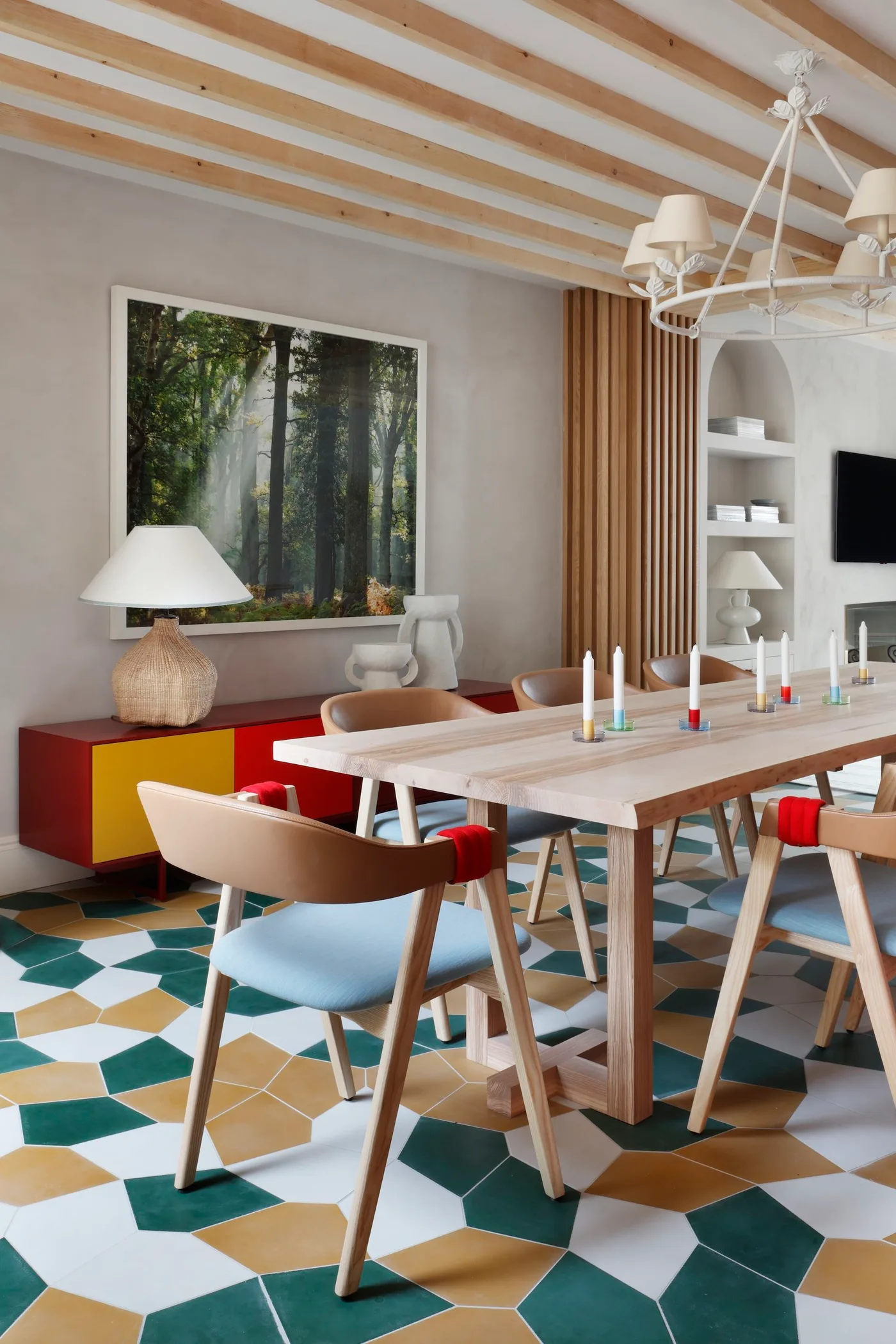 Dining room with green, ochre and white geometric flooring, pale wood table, light blue chair seats and a red-and-yellow sideboard
