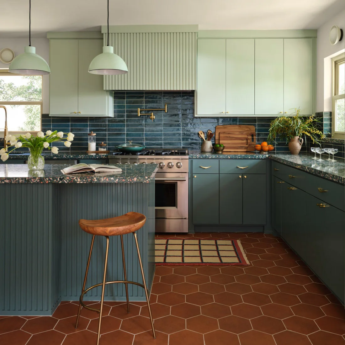 Rust-colored hexagonal floor tiles sit below two-tone green cabinets and a timber bar stool.