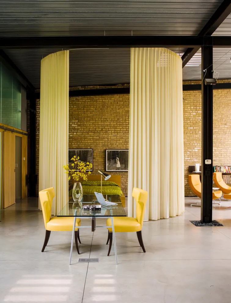 A small glass table stands beside bright yellow chairs in an industrial-style space
