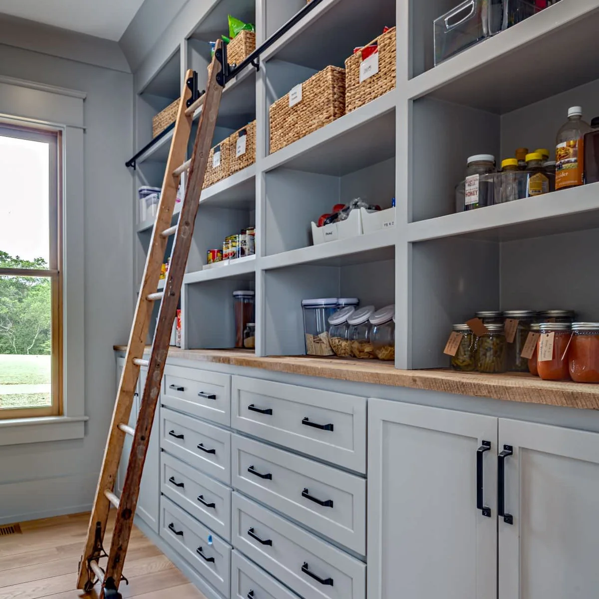 Gray pantry shelves with labeled woven baskets and a rail-mounted wood ladder