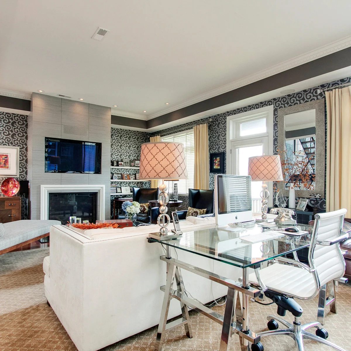 A glass trestle desk and white office chair behind a pale sofa in a patterned living room.