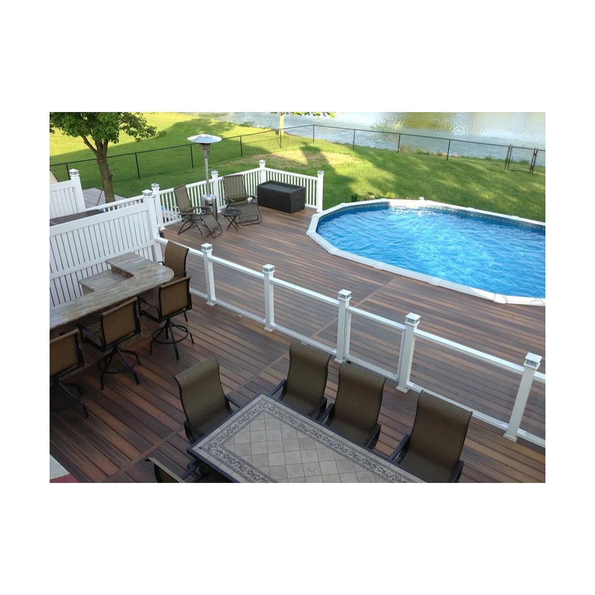 Above-ground pool beside a multi-level deck with white railings, a dining table and a smaller sitting area near the water.