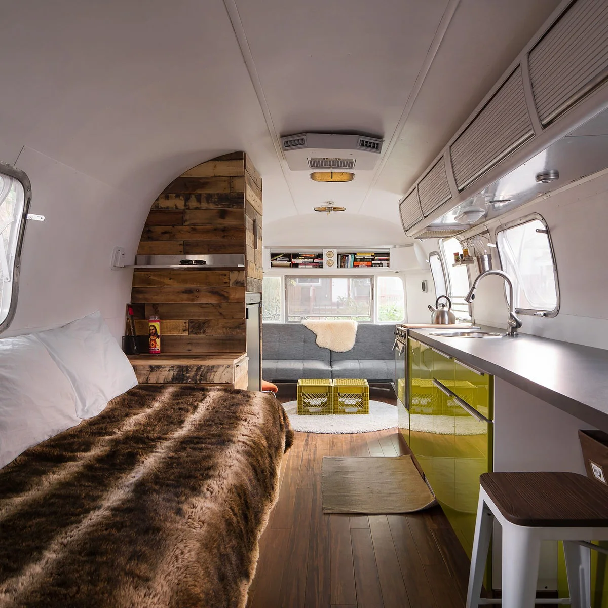Curved white camper with glossy green lower kitchen cabinets, a gray end sofa and wood-clad partition.
