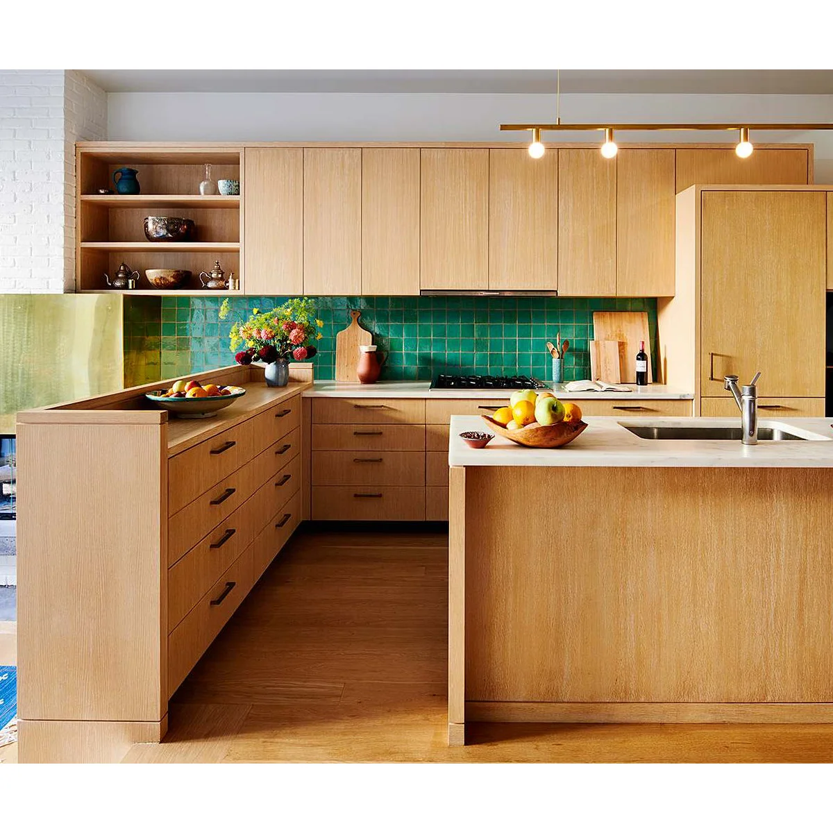 A U-shaped wood kitchen with a green tiled backsplash, open corner shelves and a pale counter at the sink.