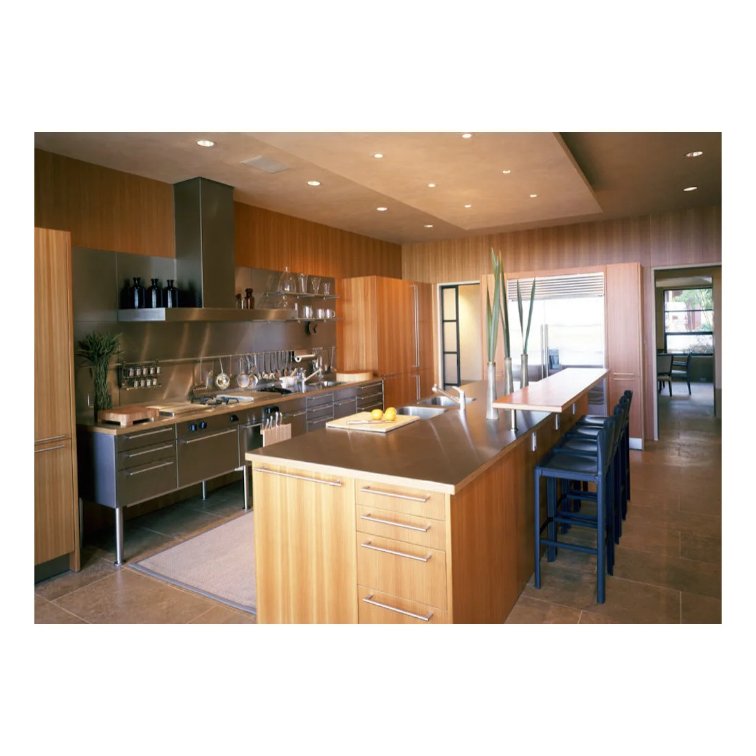 Brown tiled flooring runs through a timber-and-stainless kitchen beside a long row of dark stools.