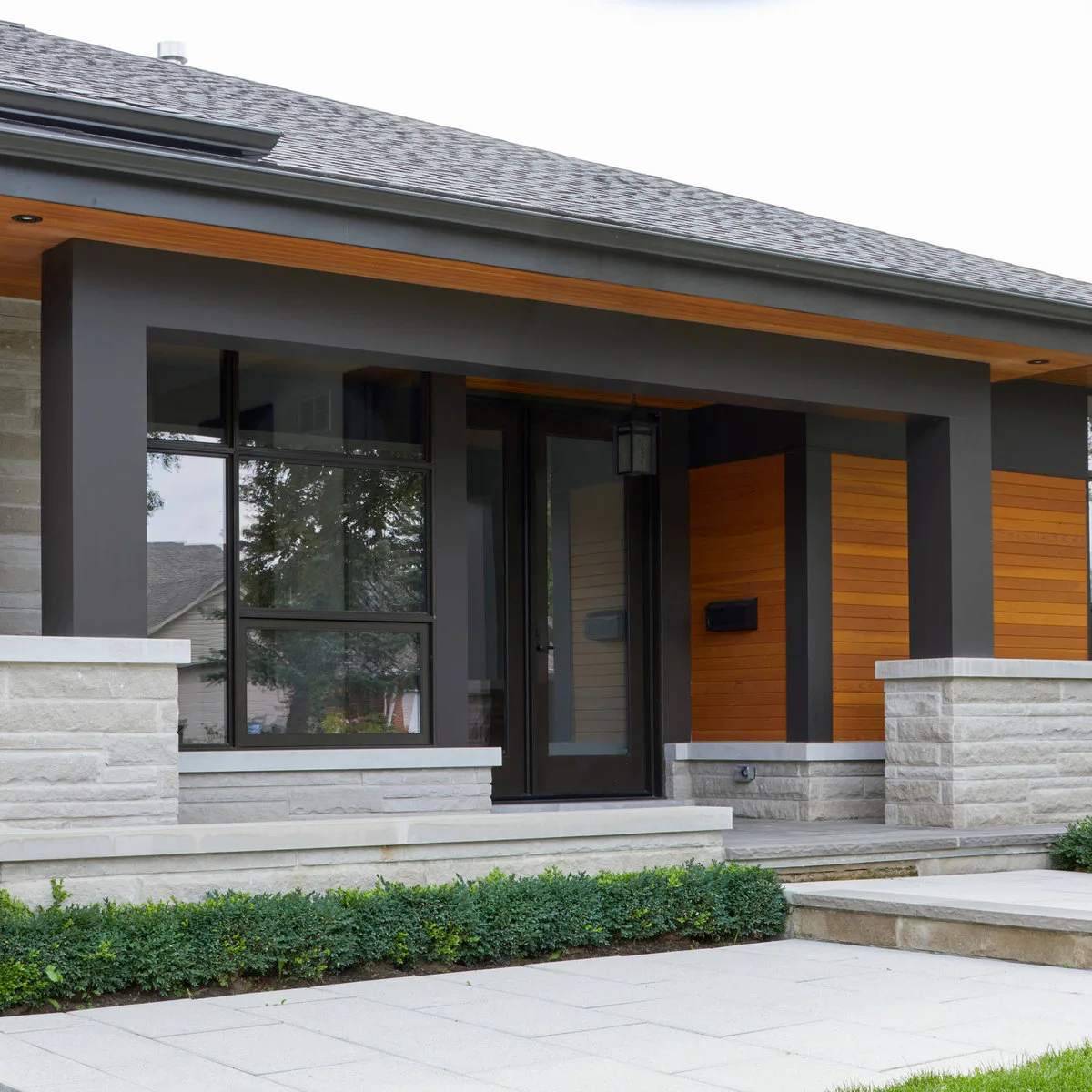 Modern front entrance with dark framing, warm wood-colored wall panels and a clear shallow landing
