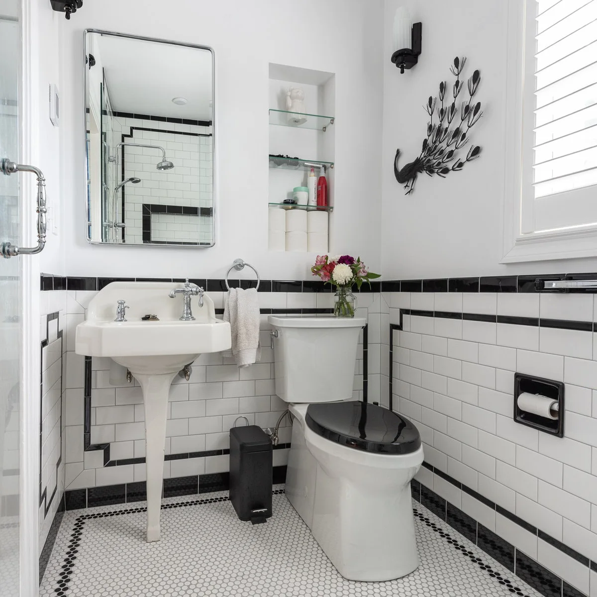 Black peacock wall sculpture above a toilet in a black-and-white tiled bathroom