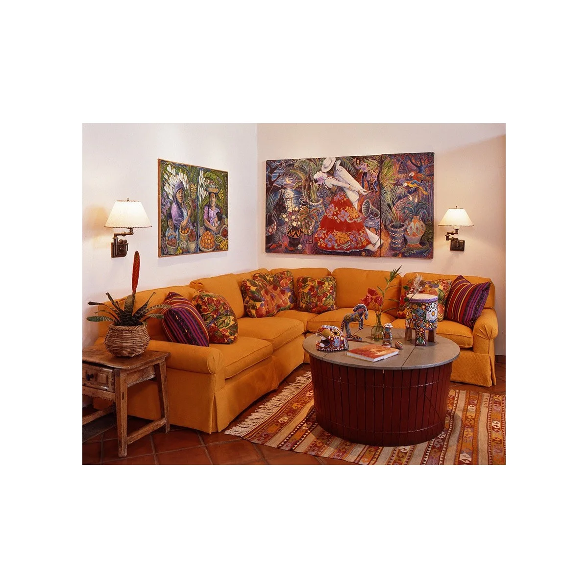 Mustard corner sofa with patterned cushions beneath colorful paintings beside a round coffee table and warm tiled floor.