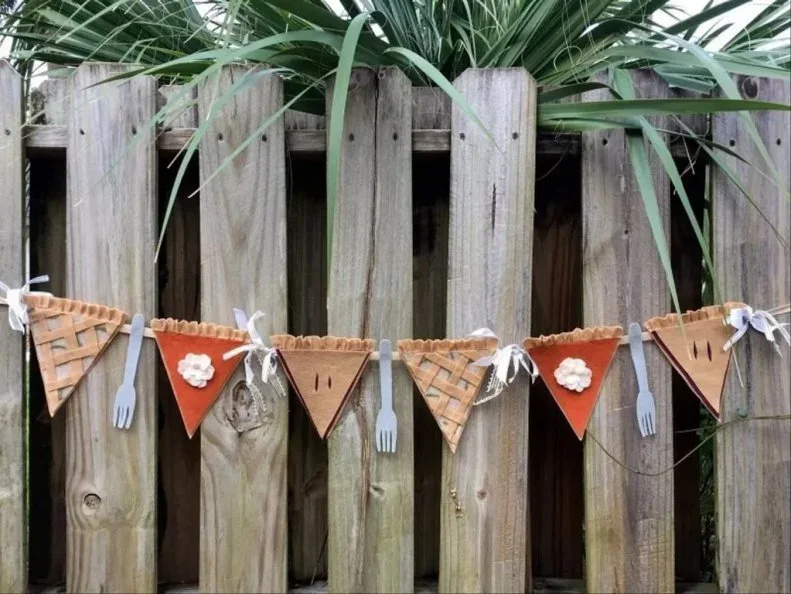 Triangular pie-slice decorations and fork shapes hang across a wooden fence with small pale ties
