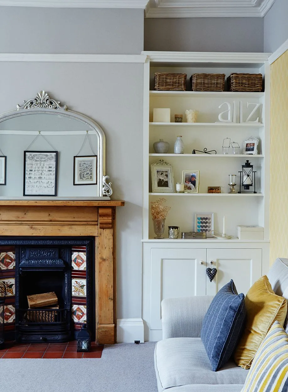 Wood mantel with ornate pale mirror, small decorative pieces and white built-in shelves beside tiled fireplace