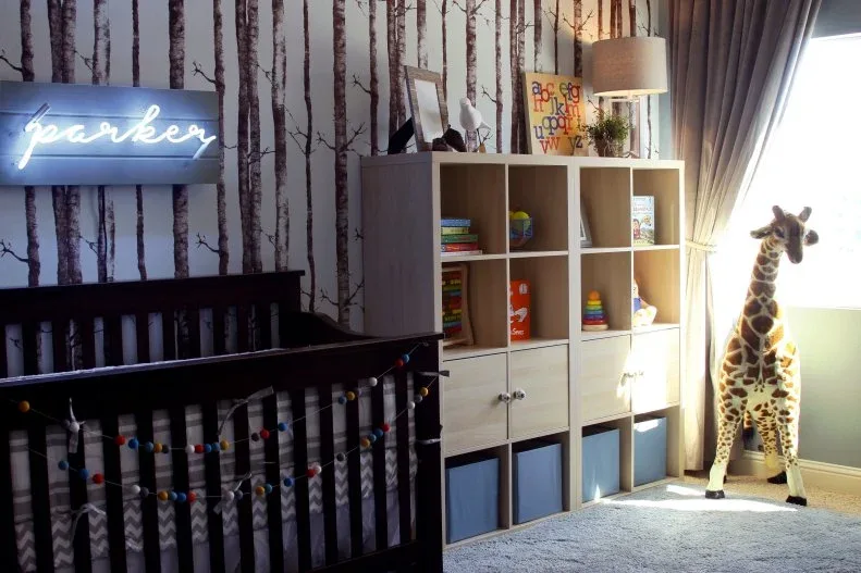 Dark crib and pale cubby storage against tree-patterned wall with blue containers and decorative giraffe.