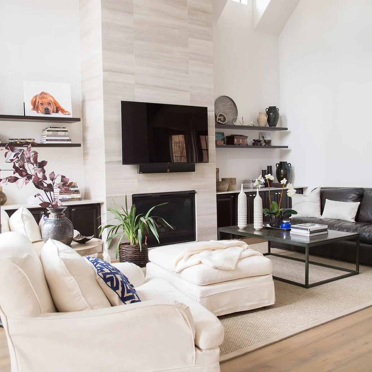 A white chaise sofa faces a dark sofa across a black-framed table, with a fireplace between the built-in shelves.