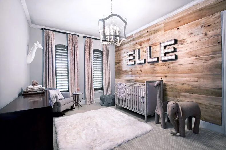 Nursery with broad wooden wall, quieter crib, pale adult seating, tall patterned curtains, rug and animal-shaped decorative pieces.