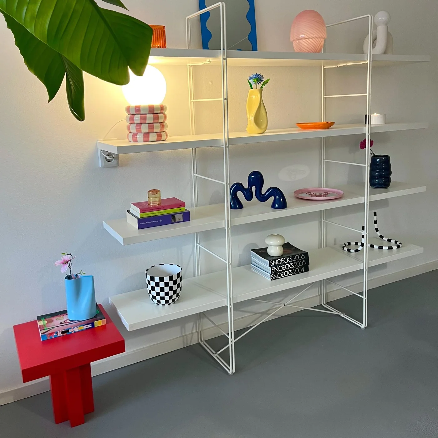 Small red side table with a geometric base beside white display shelves