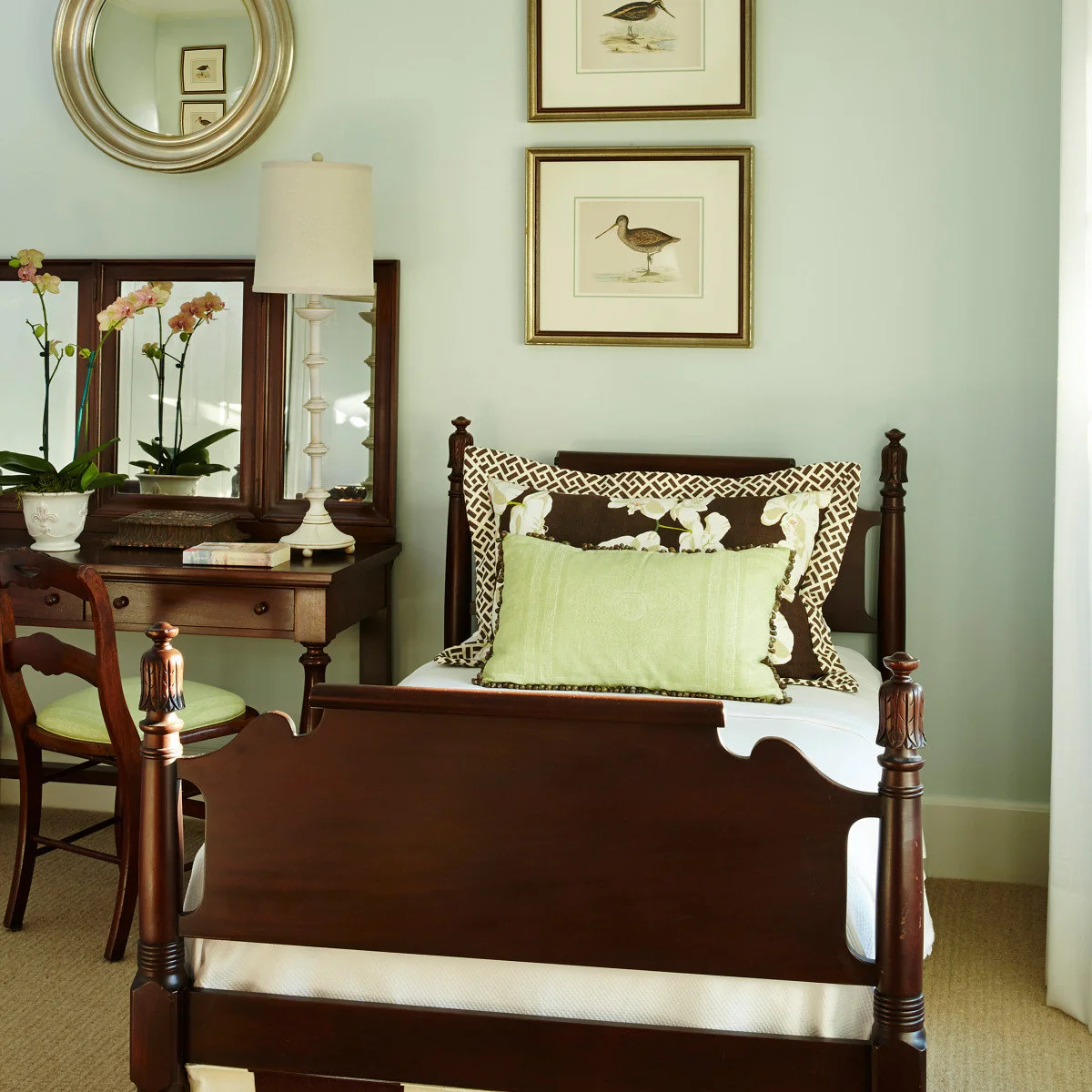 Dark family antique bed beside a writing table, framed bird prints and green pillows
