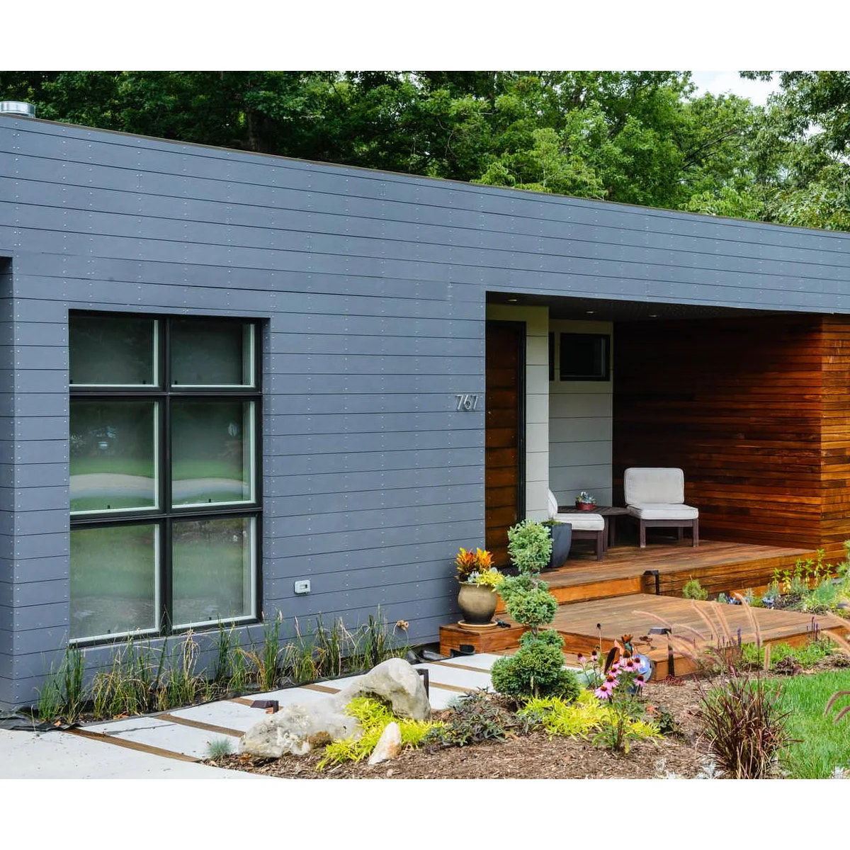 Modern recessed front porch with two pale chairs against a wood-colored wall beside the entrance