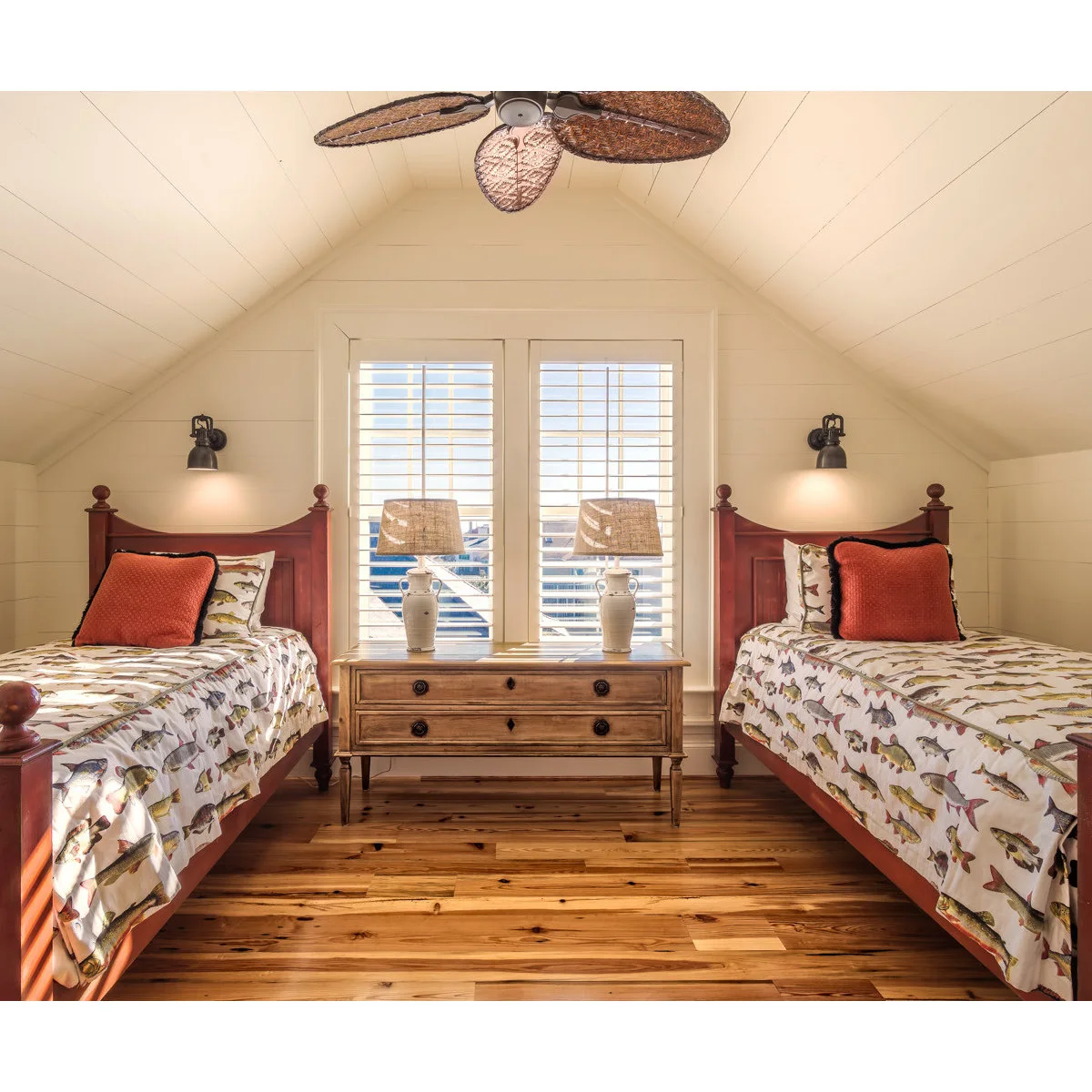 Two red wood beds beneath a sloping ceiling with fish-pattern covers and a low wood chest between them