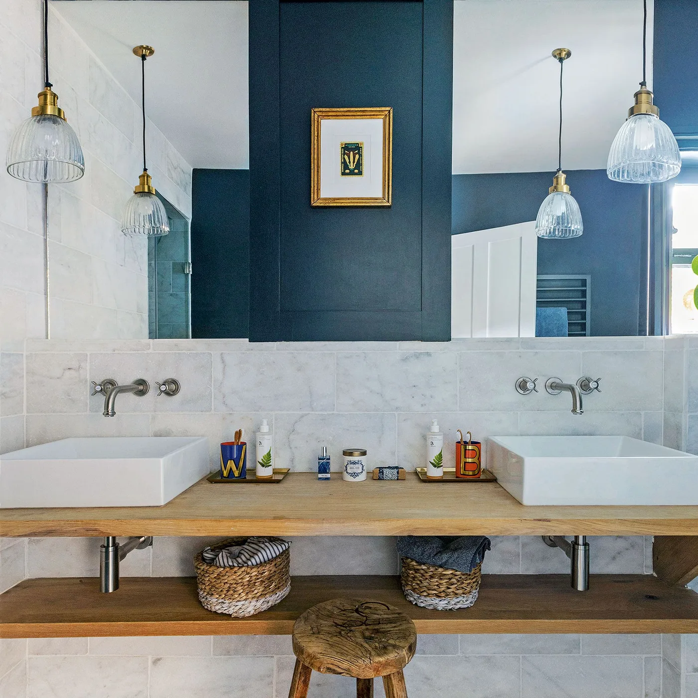 Two white vessel sinks sit on a wooden counter below mirrors reflecting a deep blue central wall