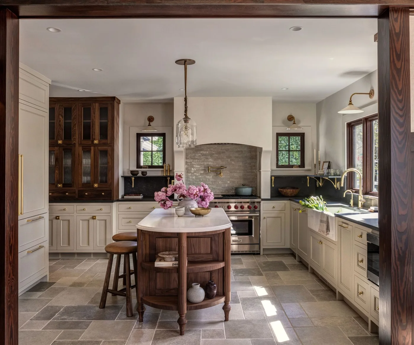 Off-white base cabinets sit beside a dark glazed timber cupboard and a rounded freestanding timber island.
