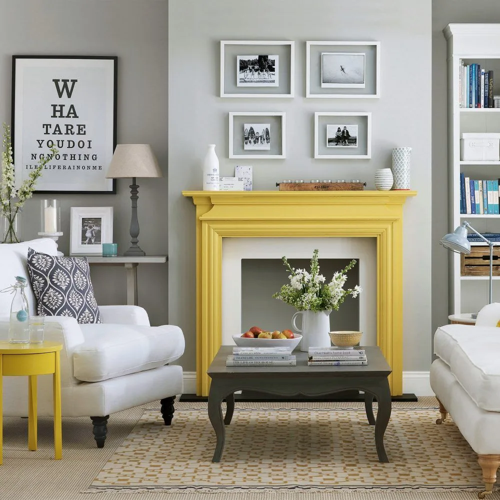 Yellow mantel with white decorative vessels, four white-framed photographs above and gray wall