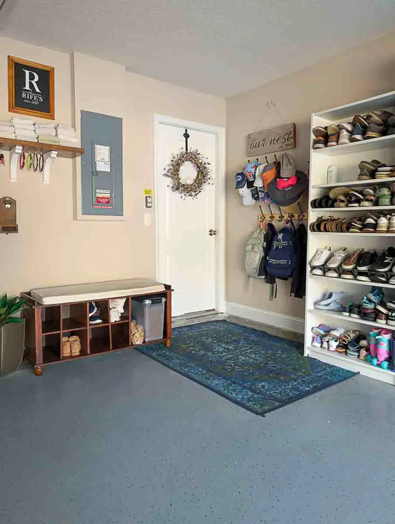 Garage entry with a dark wooden cubby bench, a tall white shoe shelf, hat racks and a blue patterned rug.