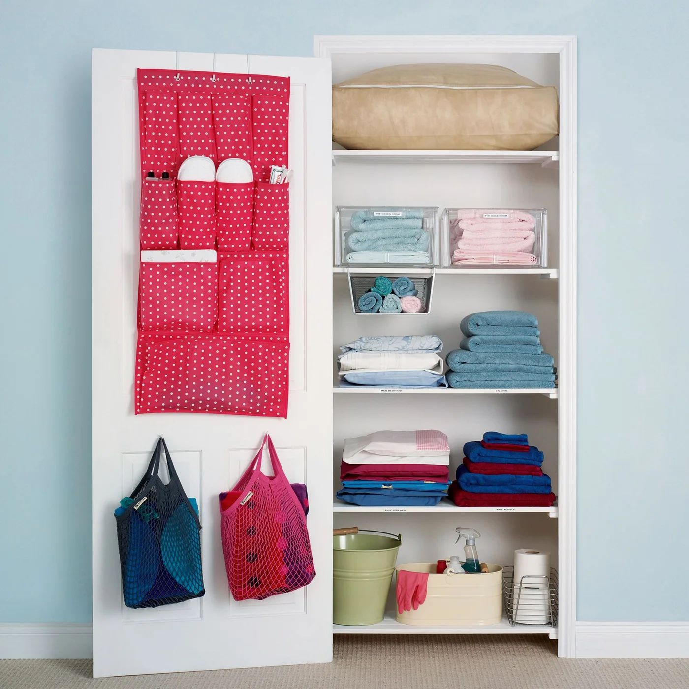 White linen closet with color-grouped towels, labeled sheet shelves and a red pocket organizer on the door