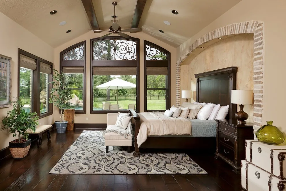 Dark brown floorboards surround a bed and patterned rug beside tall windows