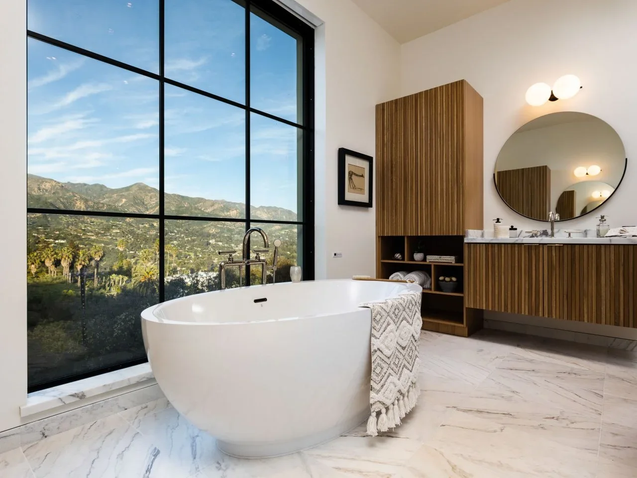 A large black-framed window rises beside a white tub and ribbed timber vanity with open shelves.