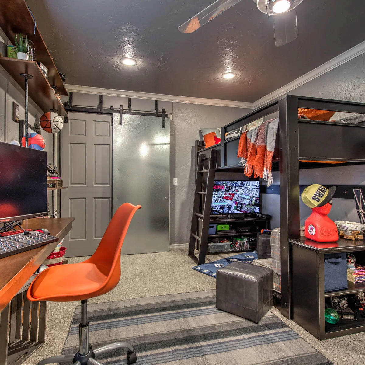 A compact bedroom with a wood loft bed, an orange chair, a television and shelves holding games and small objects.