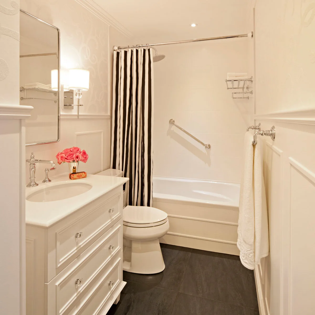 White panel molding and a white vanity with clear knobs accompany a black-and-white striped shower curtain and dark floor.