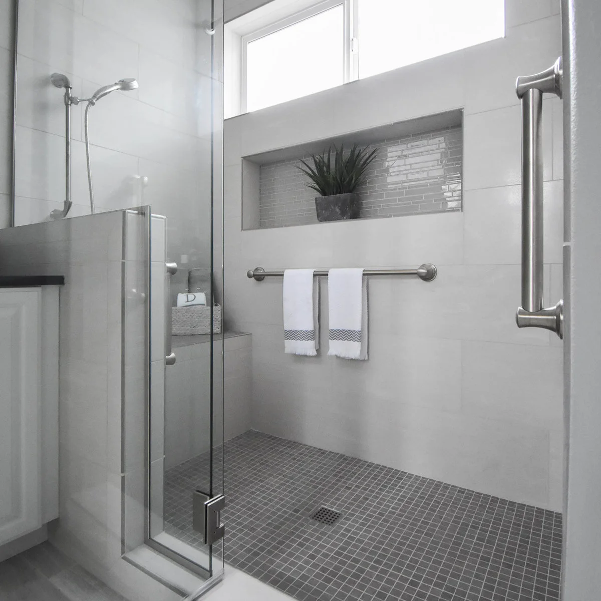 Glass shower door beside a half wall with gray floor mosaics and a horizontal niche