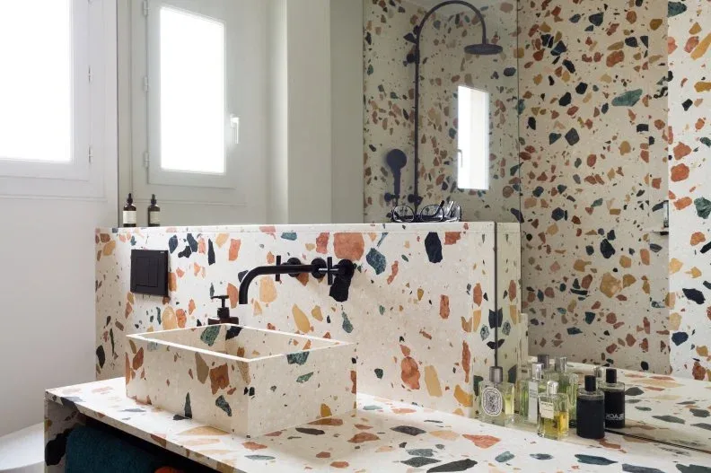 Large colored chips cover a bathroom basin, counter and shower wall beside black fittings.