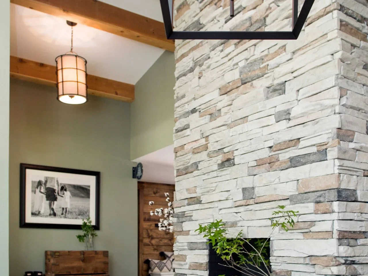 A tall stacked-stone fireplace rises beneath timber ceiling beams beside a large dark-framed lantern.
