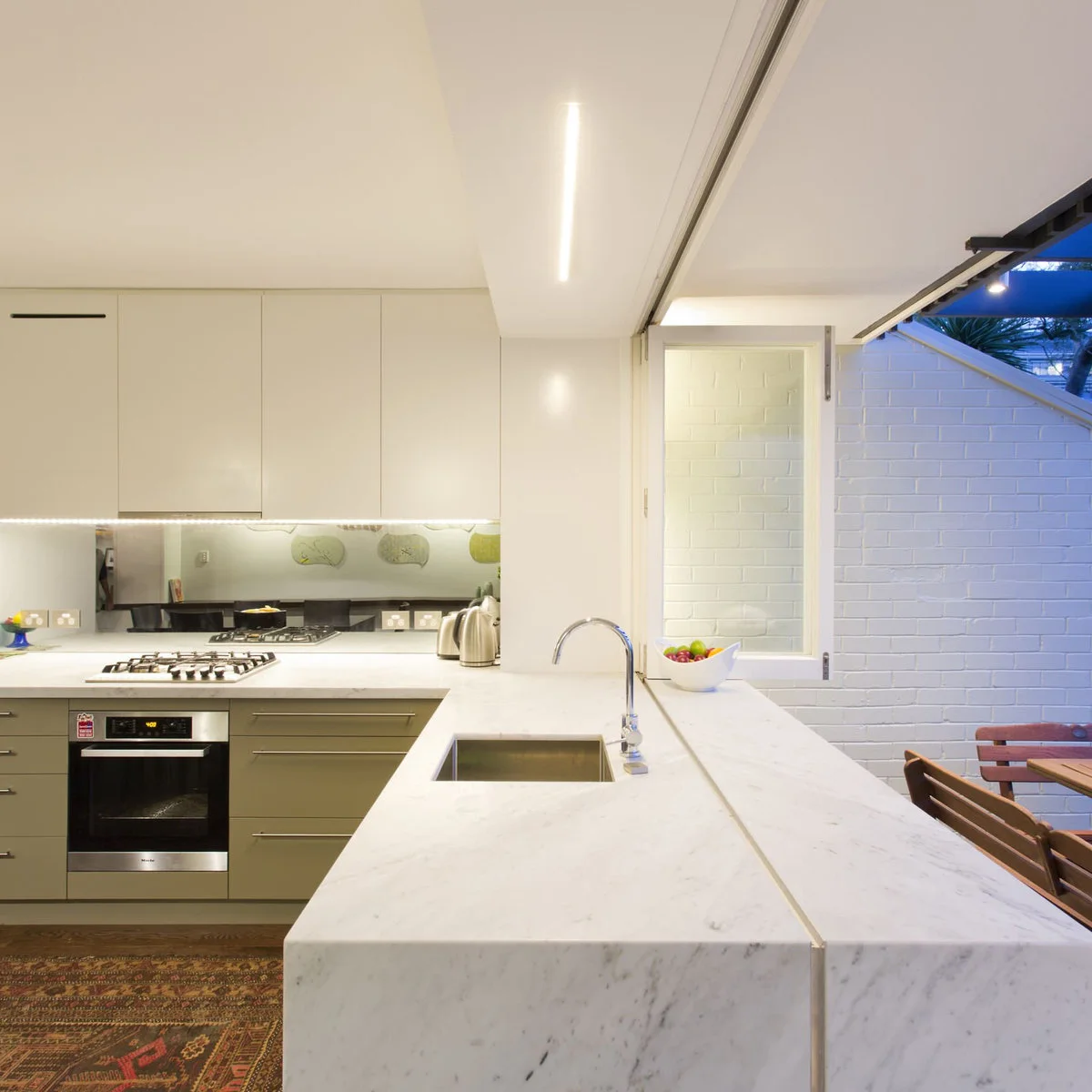 Terrace-house kitchen with a pale sink counter continuing toward an opening to outdoor seating