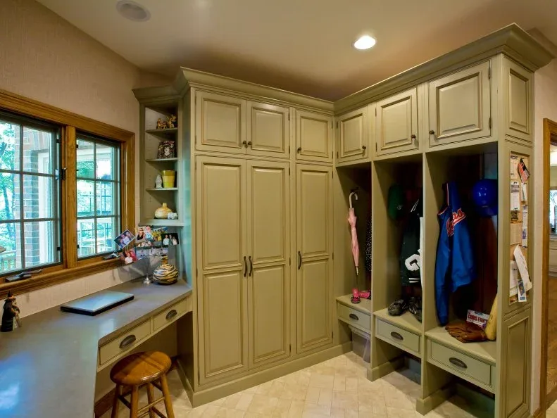 Olive-toned cupboards include two open coat bays with small bench seats and drawers, beside a window counter.