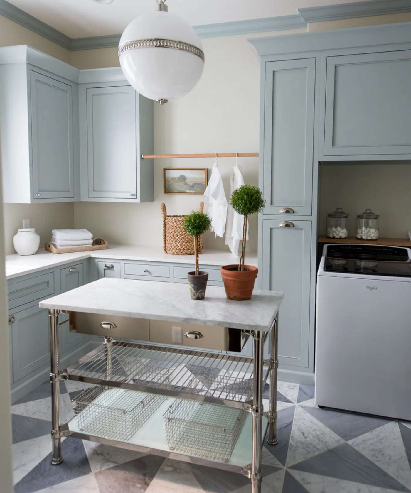 Blue-gray laundry cabinets with small metal-framed worktable, checked floor, hanging rail and white pendant