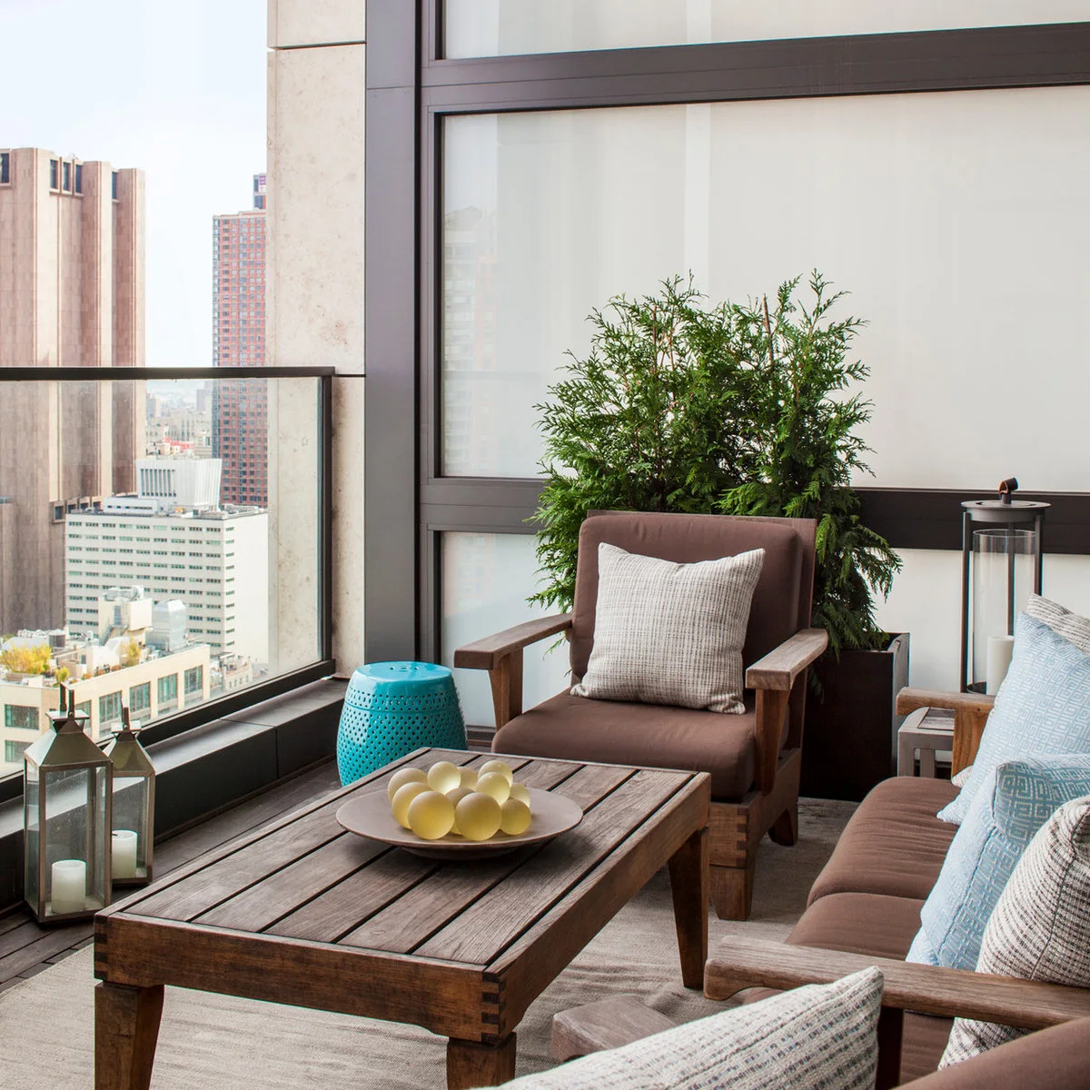Apartment balcony with brown-cushioned wood-framed seats, rectangular table and tall planter